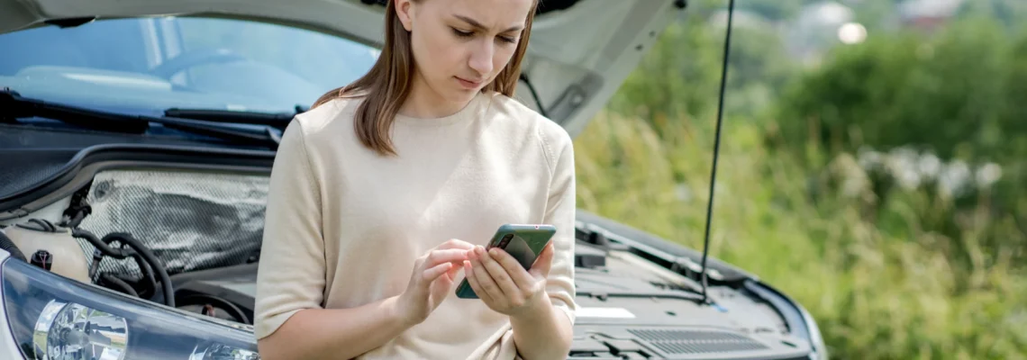 How To Get An Emergency Car Repair Loan NZ; woman using phone stands next to broken down car | Swoosh NZ