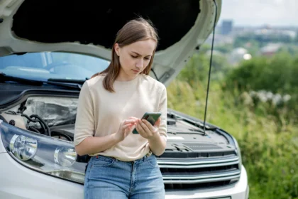 How To Get An Emergency Car Repair Loan NZ; woman using phone stands next to broken down car | Swoosh NZ